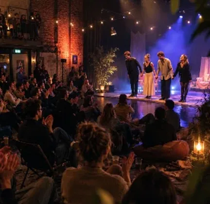 An audience in a small theatre, the stage lit in red and blue